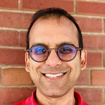 Sacha Agrawal smiling in front of a brick wall.